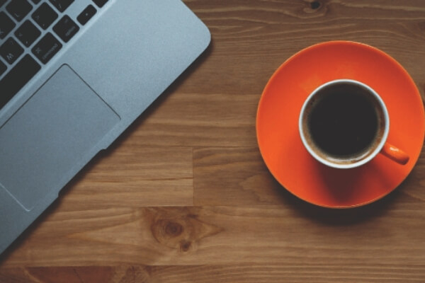 Zeigt einen Laptop und eine Tasse Kaffee